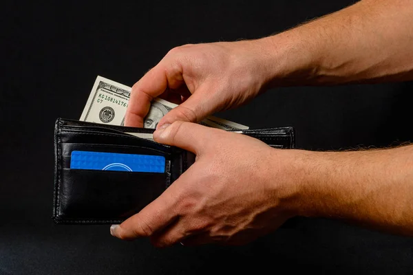 Black wallet with dollars in man hands on black background. — Stock Fotó