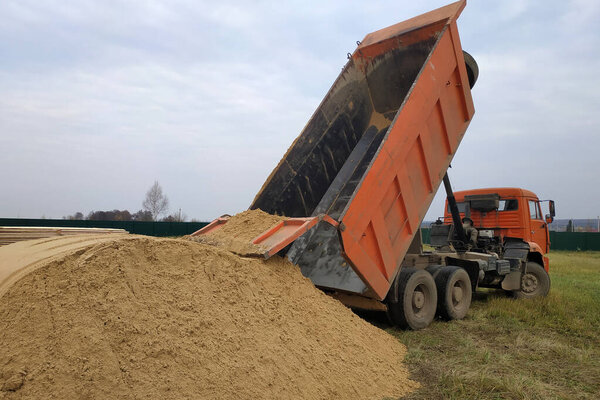 A large orange dump truck unloads the sand.2020
