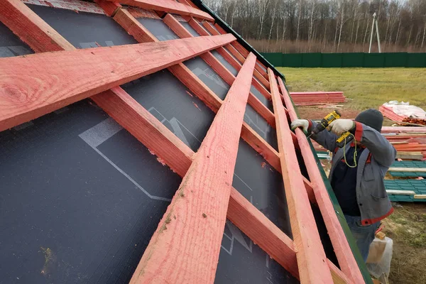 The roof is covered with insulating material, the base of the roof. Worker hammering boards to the base of the roof.2020