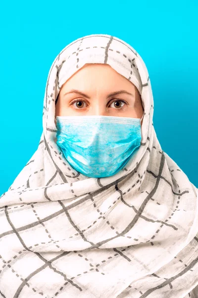 Cheerful woman on blue background in scarf and medical mask.2020