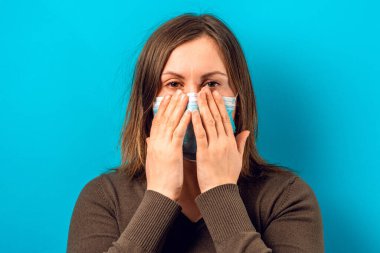 Mavi arka planda bir maskeyle tatmin olmamış bir kadının portresi. 2020