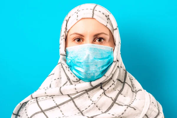 Cheerful woman on blue background in scarf and medical mask.2020