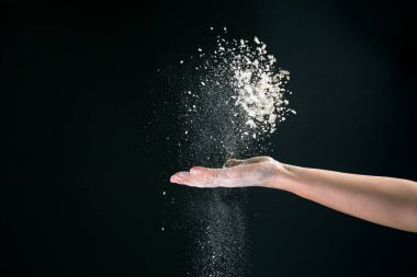 Siyah arka planda, bir kadının eli 2020 'de pişirmek için kar gibi beyaz un döker.
