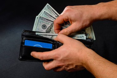 Siyah arka plandaki adam elinde dolarlarla dolu bir cüzdan tutuyor.