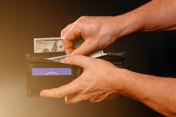 Man on black background holds in his hands a wallet with dollars close up.2020