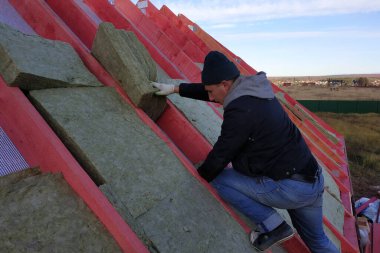 İşçi çatıya mineral yünü koyar ve evi yalıtır. 2020