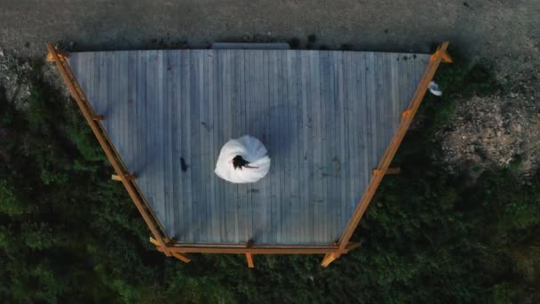 El novio sostiene a la novia en sus brazos y gira en un baile de bodas en una plataforma de observación en las montañas. Vista aérea . — Vídeos de Stock