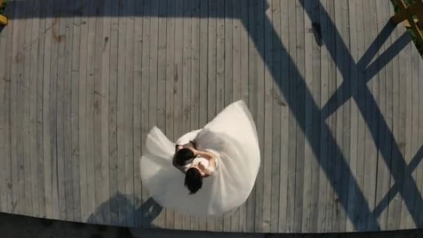 Groom holds the bride in his arms and whirls in a wedding dance on a viewing platform in the mountains. Aerial view. — Stock Video