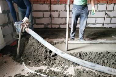 The worker performs a sand-cement floor screed above the floor heating.2020