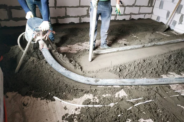 The worker performs a sand-cement floor screed above the floor heating.2020
