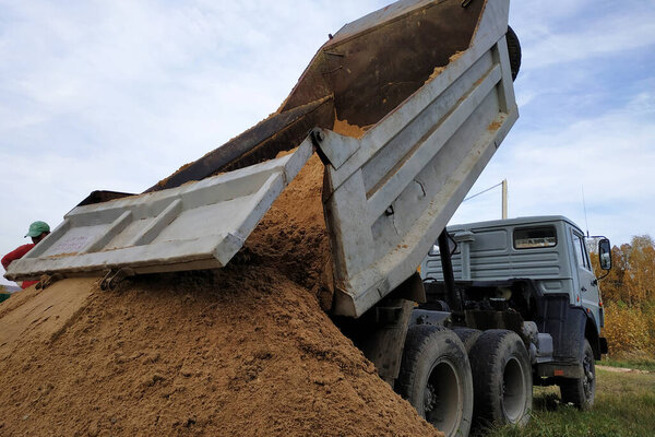 A dump truck unloads sand at a construction site to mix cement.2020