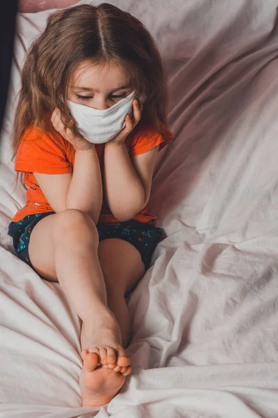 Niña Con Máscara Médica Pijamas Coloridos Sentada Cama Casa Durante — Foto de Stock