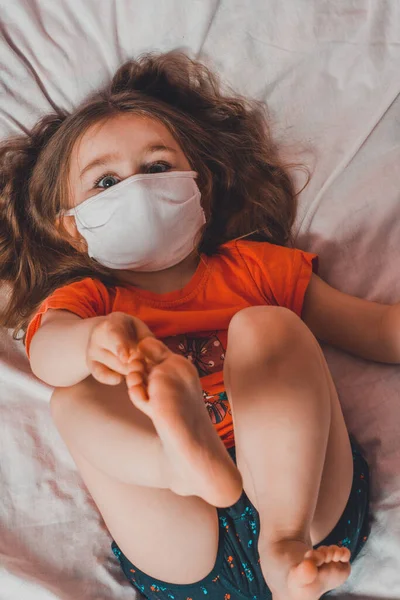 Mała Dziewczynka Ciemnymi Włosami Leżąca Łóżku Masce Medycznej Podczas Choroby — Zdjęcie stockowe