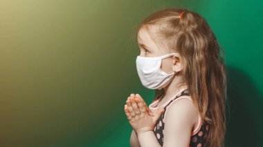 Coronavirüs salgını sırasında maske takan beyaz hasta bir kız yeşil arka plan için dua ediyor..