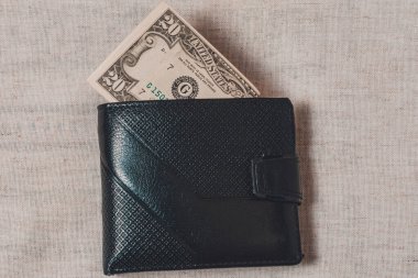 Gri bir arka planda koyu deri bir cüzdanın içinden çıkan 20 dolar.