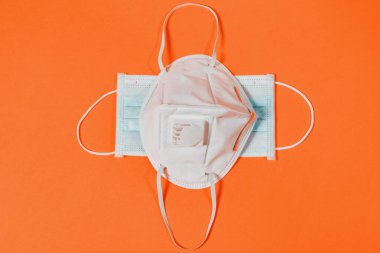 Turuncu arka planda kapakçık ve cerrahi maskeli tıbbi maske 2021. Haç şeklinde maskeli kavramsal fotoğraf 2021 salgınlarında hastalıklara ve çeşitli virüslere karşı korunmanın bir sembolü.