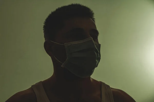 loseup of face male patient in medical mask on self isolation during coronavirus pandemic. Silhouette photo of patient in dark room. The concept of fear and despair 2021