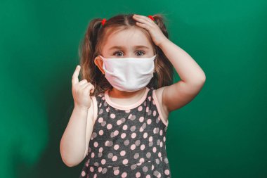 Tıbbi maskeli küçük bir kızın yeşil arka planı gösteren kavramsal fotoğrafı. 2020 'de yakın plan.