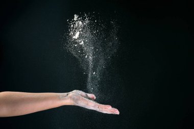 Siyah arka planda, bir kadının eli 2020 'de pişirmek için kar gibi beyaz un döker.