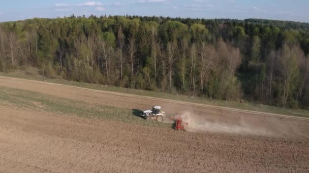 Een boer kweekt een akker op een rupstrekker en laat de grond los met een schijfcultivator tegen de achtergrond van bos en blauwe lucht. 4k-beelden. — Stockvideo