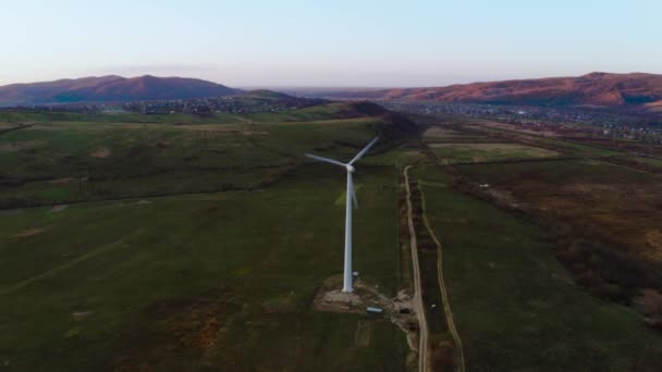 Molino de viento blanco solitario gira al atardecer en las montañas produciendo energía limpia — Vídeo de stock