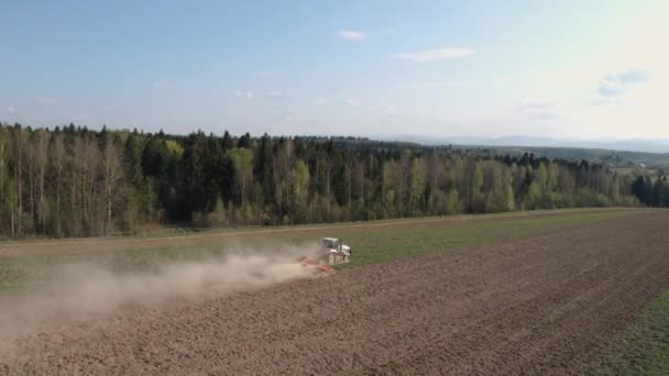 Un agricoltore coltiva un campo su un trattore cingolato e allenta il terreno con un coltivatore di dischi sullo sfondo della foresta e del cielo blu. 4k filmati . — Video Stock