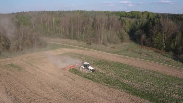 Rolnik uprawia pole na ciągniku gąsienicowym i rozluźnia glebę kultywatorem tarczowym na tle lasu i błękitnego nieba. Materiał 4k. — Wideo stockowe