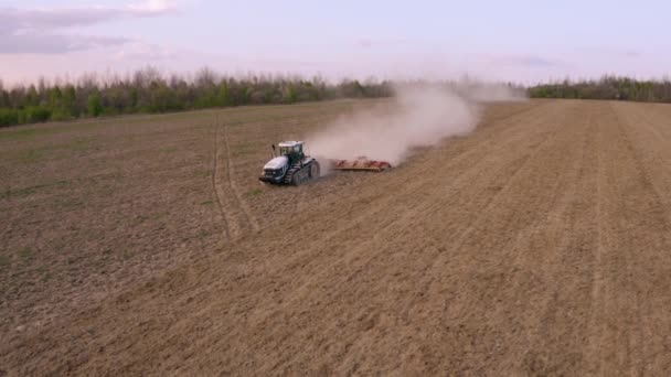 Vista lateral de una aeronave sobrevolando un campo cultivado por un tractor sobre orugas durante una crisis en el sector agroindustrial — Vídeos de Stock