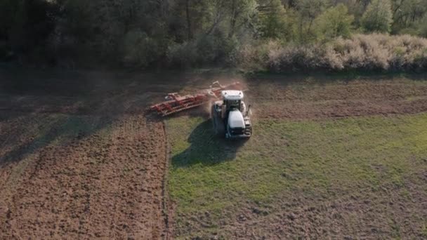 Boven het zicht van een veld vliegen op een drone tijdens het zaaien in het voorjaar, wanneer een kruipende trekker slijpt de bodem met een cultivator in tijden van economische crisis — Stockvideo
