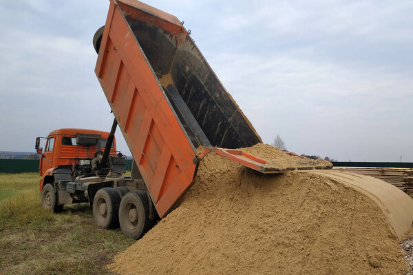 A large orange dump truck unloads the sand.2020