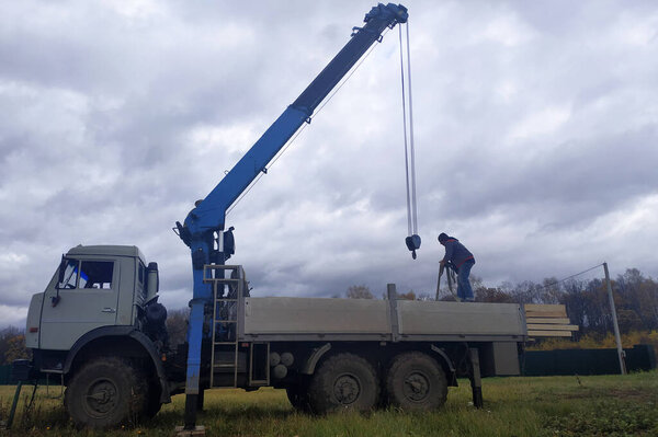 Crane on sky background unloads boards at construction site.2020