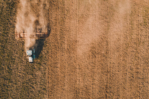Над видом поля, летящего на беспилотнике во время посева весной, когда трактор-ползун шлифует почву с культиватором во время экономического кризиса 2021 года
