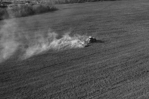 A crawler tractor cultivates the soil in an agricultural field. Top view flying on a drone. Diagonal angle in black and white color.