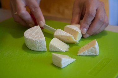 Yumuşak süt peynirini yeşil bir tabakta dilimleyen bıçak. Tabağın hazırlanışının fotoğrafı.