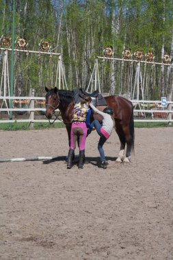 Novosibirsk, Rusya - 10 Mayıs 2015: Binicilik dersi - bir çocuğa ata binmeyi öğretmek, ilk ders, ata binen bir kız, bir eğitmen