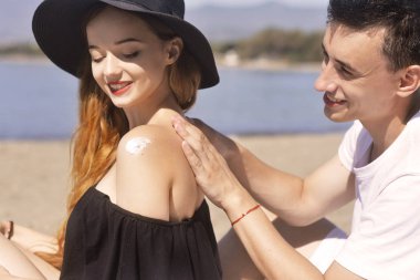 Yaz plaj tatil SunCare çift yüksek spf güneş kremi ile iyi cilt bakımı var. Çift suncream uygulanıyor. Yakışıklı adam kız plajda güneş tan losyon koyarak. Tatil, turizm.