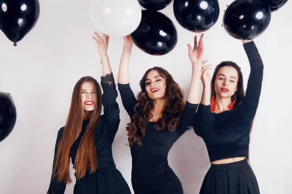 Crazy party time of three beautiful stylish women in elegant evening casual black dress celebrating , having fun, dancing on white background. Best friends girls with black and white balloon .