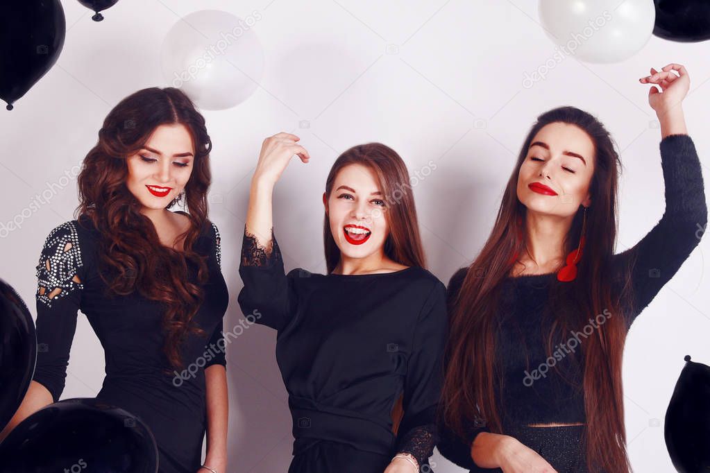Crazy party time of three beautiful stylish women in elegant evening casual black dress celebrating , having fun, dancing on white background. Best friends girls with black and white balloon .