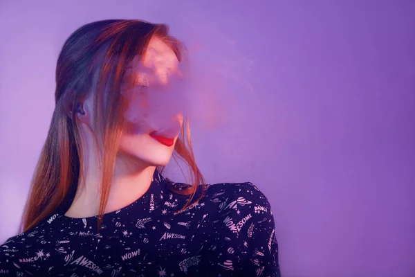 Sexy woman is vaping. Studio shooting. Fashion art portrait of beauty model woman in bright lights with colorful smoke. Smoking girl, Close up of a female inhaling from an electronic cigarette.