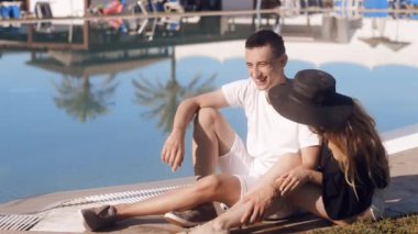 Yüzme Havuzu dinlenme kaygısız severler. Güneş gözlüğü ve şapka kız. Güneşlenme, rahatlatıcı tatil, çift. Beackground avuç içi ve Havuzu. Tatil, turizm, hooneymoon. Gülümse, lought, konuşmak.