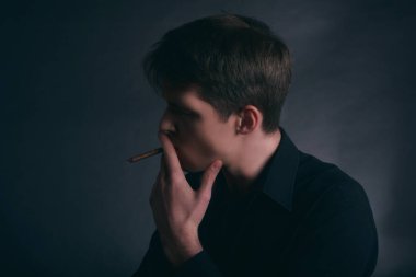 Adam bir puro sigara içiyor. Koyu arka plan üzerinde çocuk sigara sigara.
