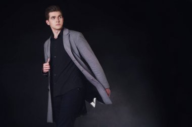 Yakışıklı delikanlı paltolu. Gri şık ceket poz moda iyi giyimli adam portresi. Siyah arka plan üzerine kendine güvenen ve odaklı bir çocuk. Mükemmel saç modeli olan zarif adam. Erkek saç şekillendirme.
