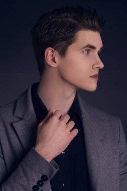 Yakışıklı delikanlı paltolu. Gri şık ceket poz moda iyi giyimli adam portresi. Siyah arka plan üzerine kendine güvenen ve odaklı bir çocuk. Mükemmel saç modeli olan zarif adam. Erkek saç şekillendirme.