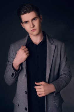Yakışıklı delikanlı paltolu. Gri şık ceket poz moda iyi giyimli adam portresi. Siyah arka plan üzerine kendine güvenen ve odaklı bir çocuk. Mükemmel saç modeli olan zarif adam. Erkek saç şekillendirme.