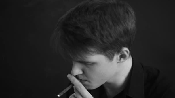 特写白人男子抽雪茄 穿着黑色衬衫 工作室肖像黑白相间 黑暗和阴沉的拍摄一个年轻人在黑色背景吸烟 — 图库视频影像