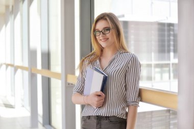 Sırt çantası ve ayakta ve üniversitede, kolaj gülümsüyor not defterleri ile neşeli çekici genç kadın. Kameraya bakarak genç sarışın işkadını veya öğrenci kız. Gözlüklü kız.
