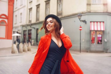 Eski şehir sokakta önünde poz şık hippi kız. Trendy genç kadın modeli. Sokak moda kavramı, şapka ve kırmızı ceket giyiyor. Turist gülümseme, güneşli bir gün. Uzun kıvırcık saçları zarif kız