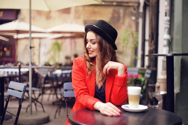 年轻时尚的美女坐在城市咖啡馆里 穿着红色夹克 街头风情 喝着芳香的咖啡 优雅的女孩在帽子微笑 甜蜜的早餐 快乐的面孔 户外的时髦人像 时尚女孩 — 图库照片