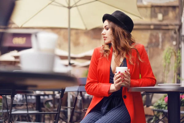 年轻时尚的美女坐在城市咖啡馆里 穿着红色夹克 街头风情 喝着芳香的咖啡 优雅的女孩在帽子微笑 甜蜜的早餐 快乐的面孔 户外的时髦人像 时尚女孩 — 图库照片