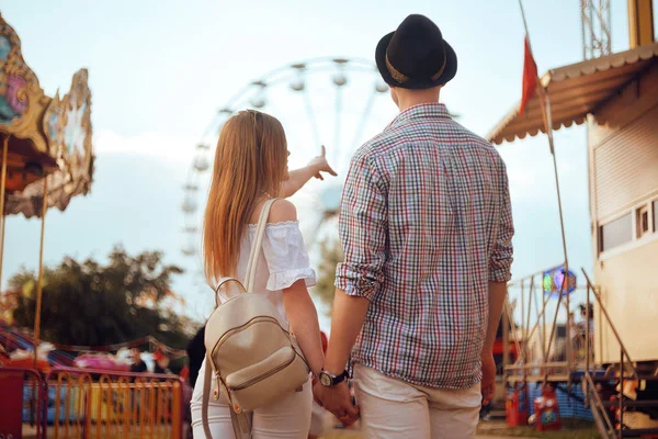 Beautiful, young couple having fun at an amusement park. Couple Dating Relaxation Love Theme Park Concept. Couple posing together on the background of a ferris wheel. Tourists have fun, smile